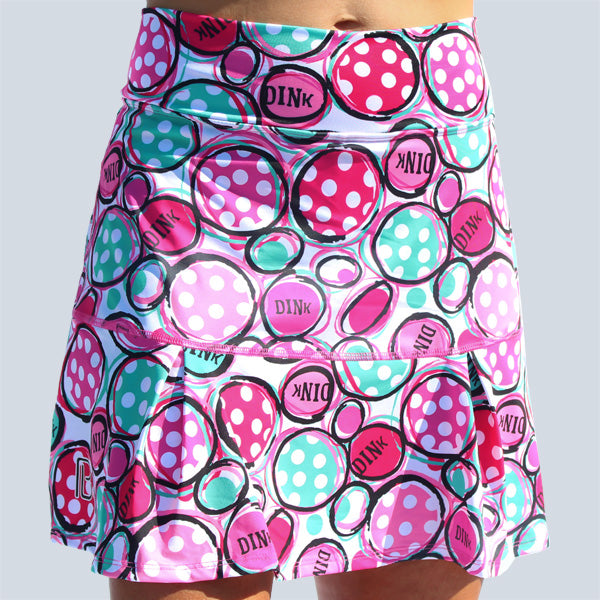 Woman models a white golf skort with a pink and green polka dot pattern and "DINK" printed throughout.