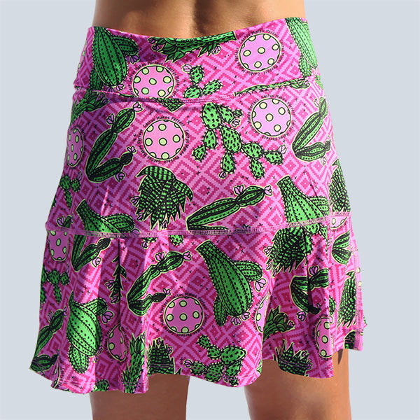Woman modeling a pink athletic skirt with a playful green cactus and pickleball print.