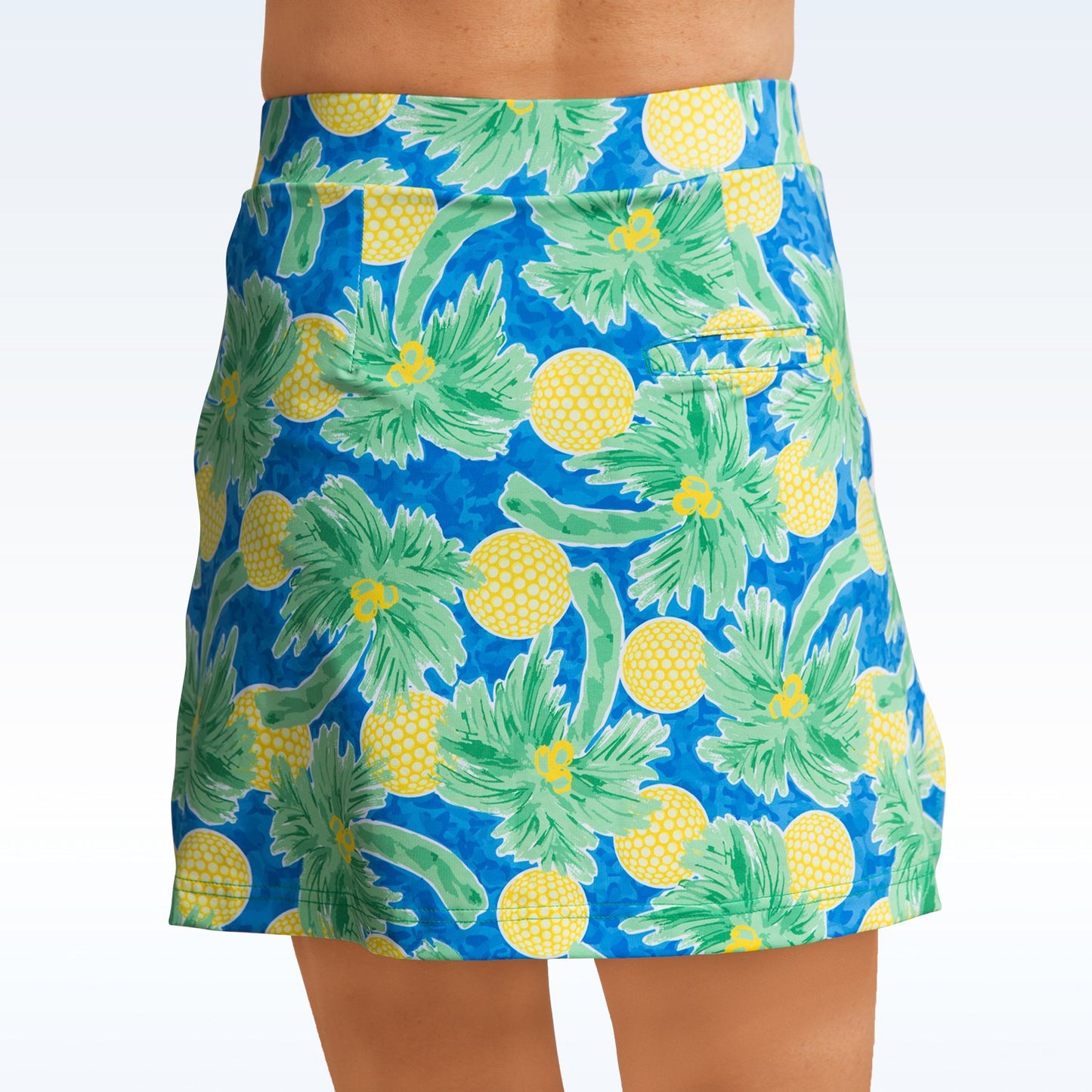 Woman models a blue golf skort featuring a playful palm tree and golf ball print.