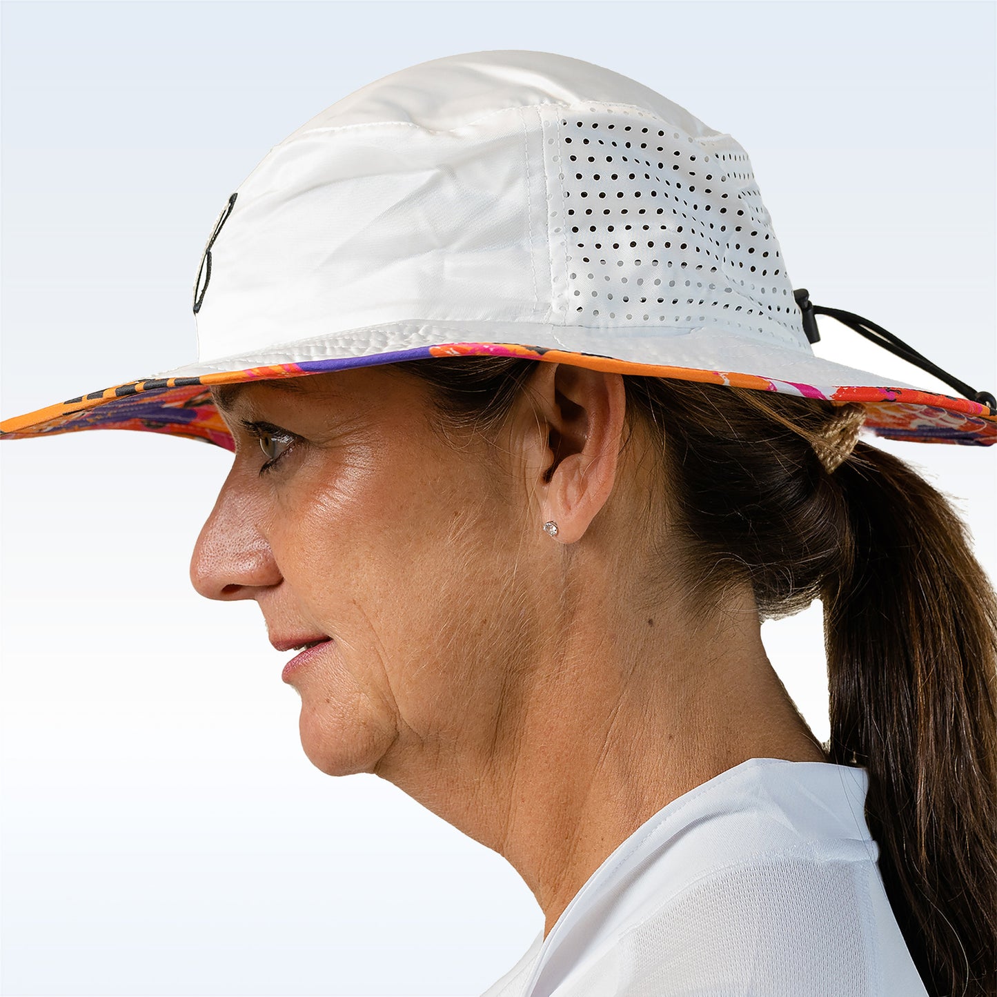 Woman models a white bucket hat with a colorful floral pattern underbrim and breathable mesh side panels.