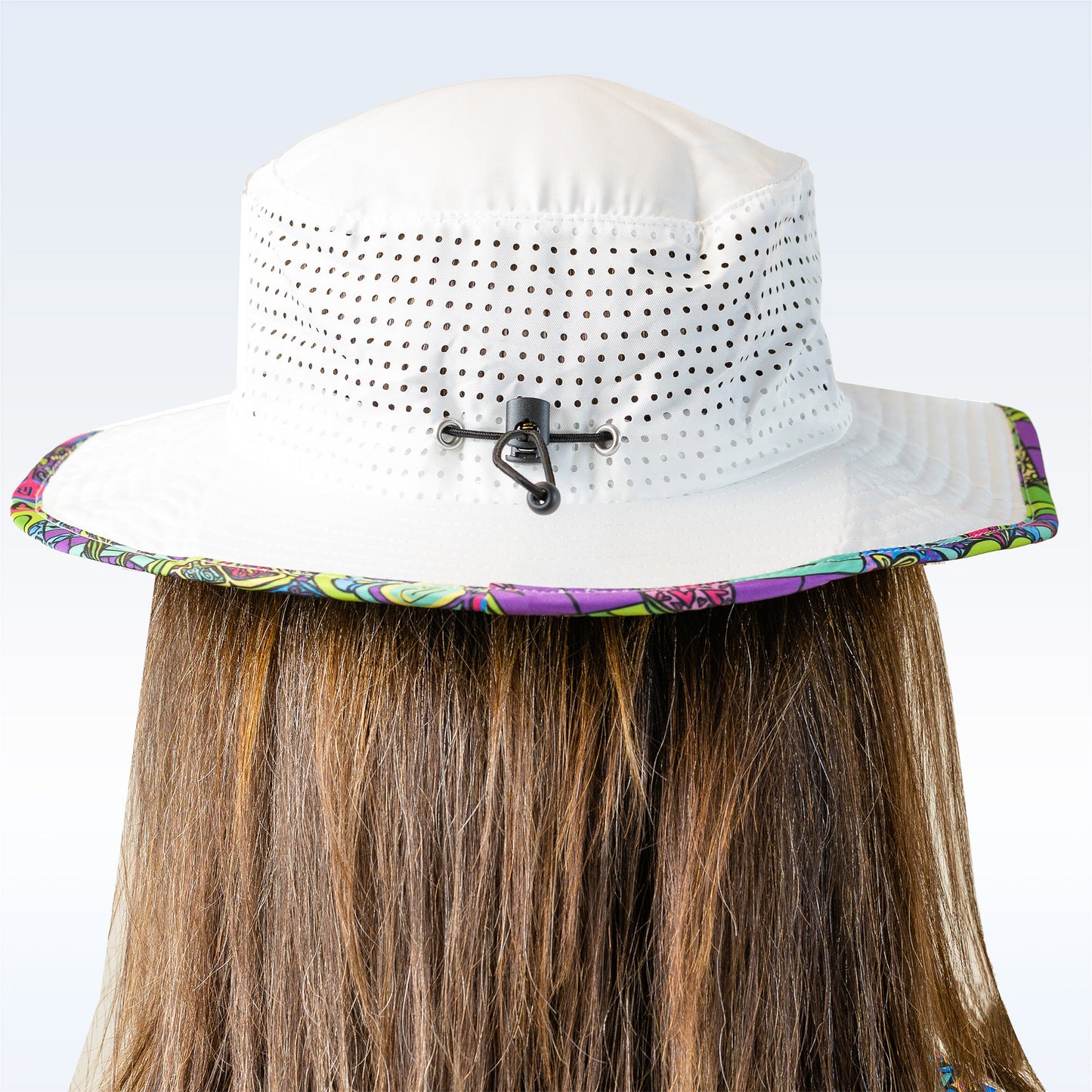 Woman models a white bucket hat with colorful patterned brim and adjustable black toggle, showcasing its breathable design from the back.