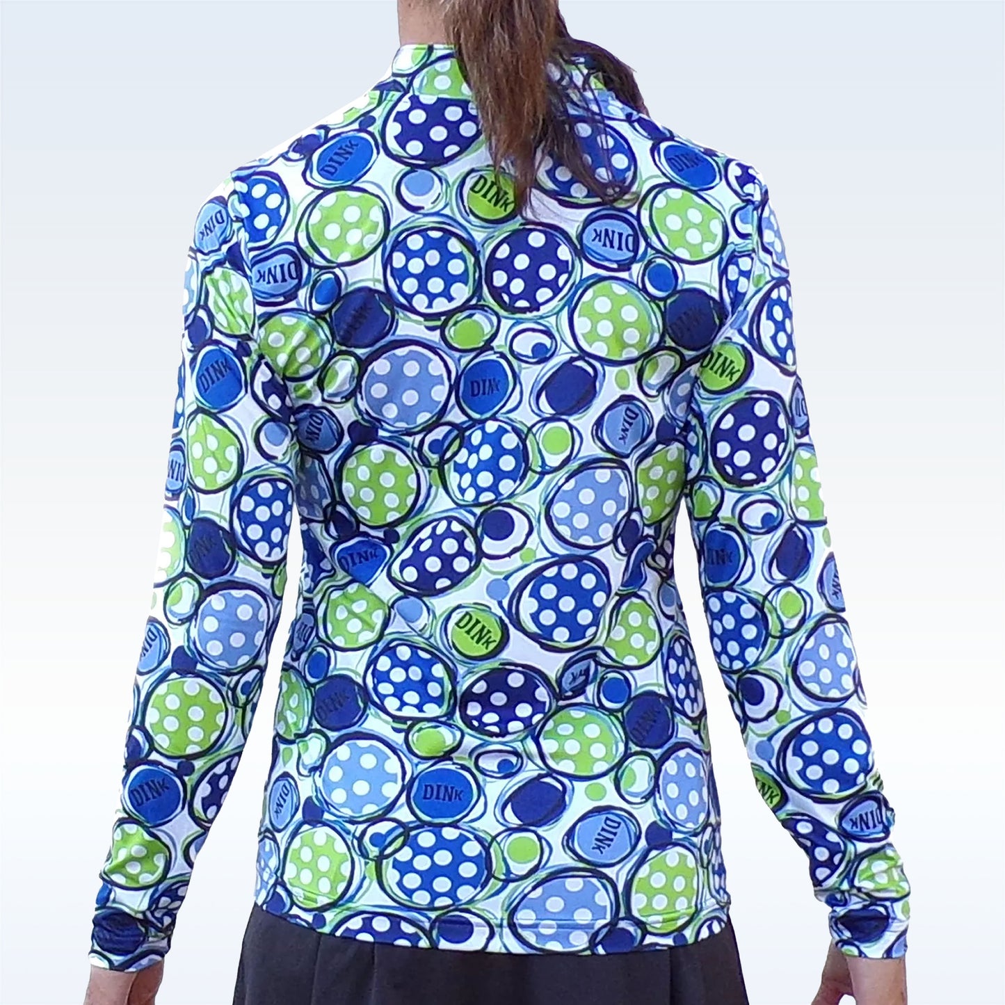 Woman models a white athletic top with a blue and green "DINK" pickleball pattern.