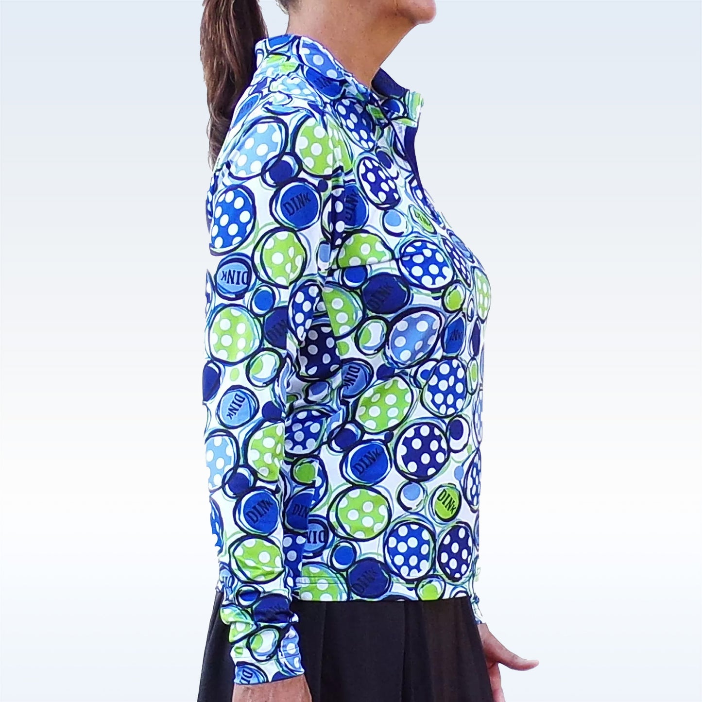 Woman models a white athletic top with a blue and green polka dot pattern and a quarter-zip neckline.