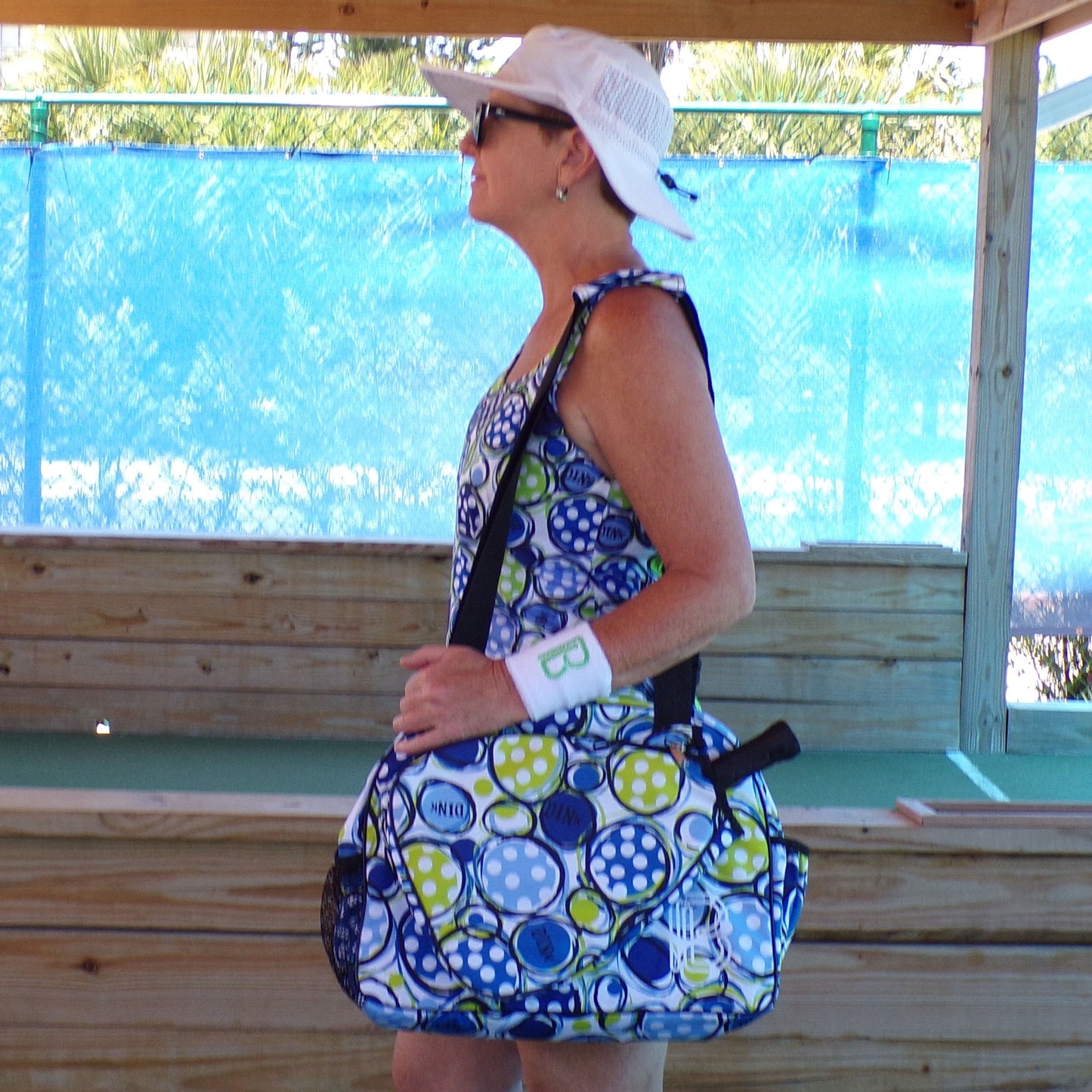 Woman carries blue and green polka dot pickleball bag on court.