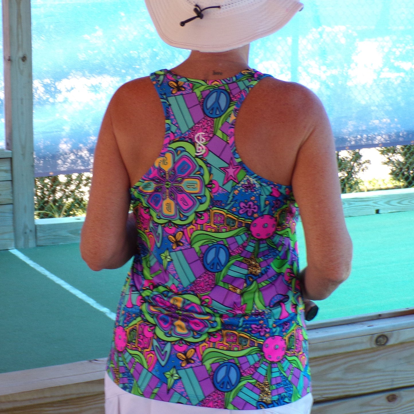 Woman models a racerback tank top with a colorful, retro-inspired print featuring peace signs, flowers, and abstract shapes.