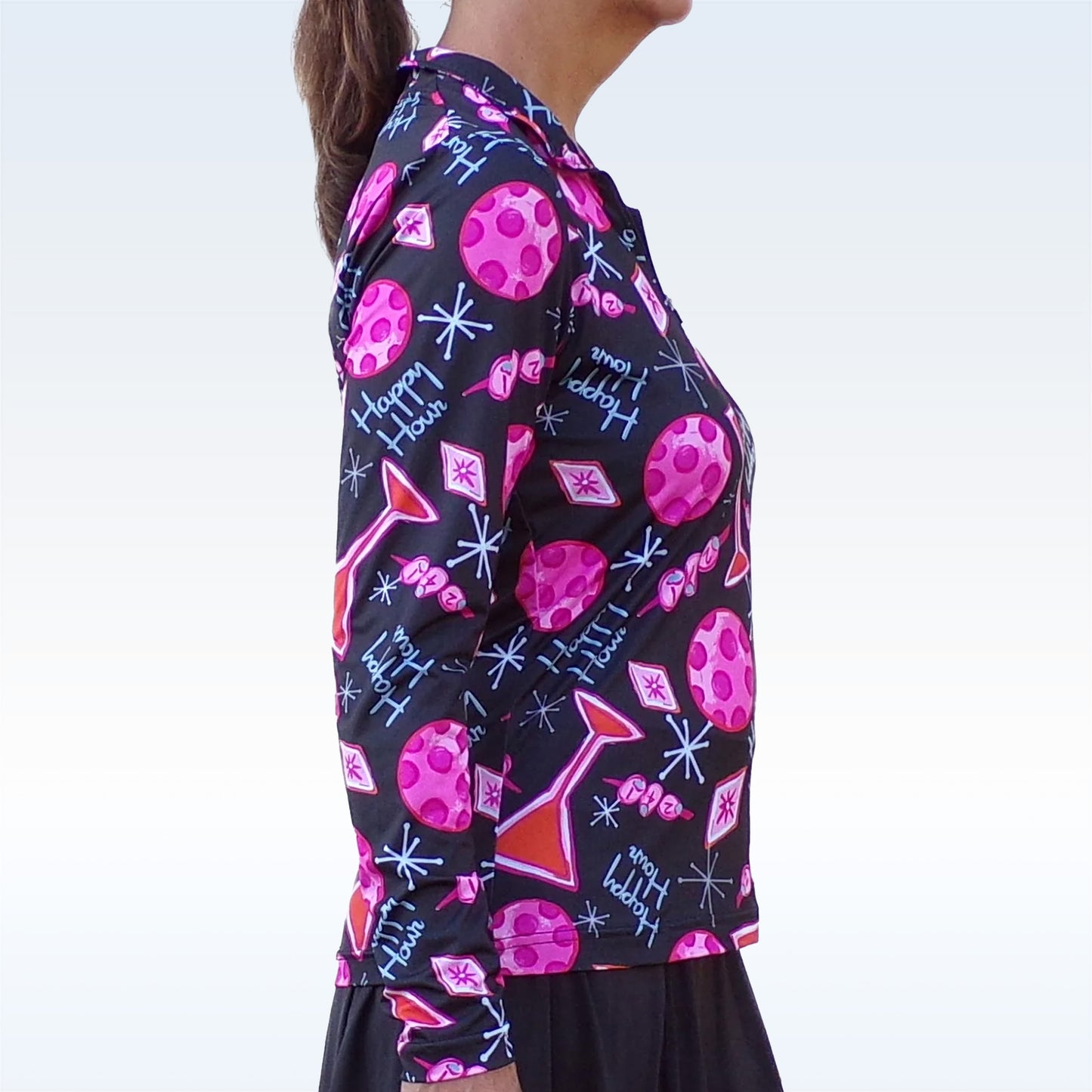 Woman models a black, long-sleeved athletic top with a playful pink "Happy Hour" cocktail and golf ball print.