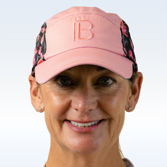 Woman smiles wearing a pink athletic cap with black floral print and embroidered "B" logo.