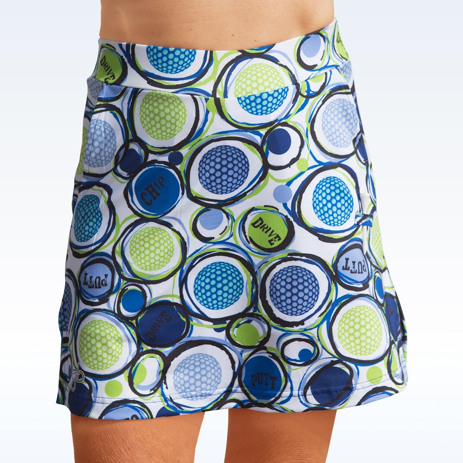 Woman models a white golf skort with a blue and green golf ball and golf term pattern. 
