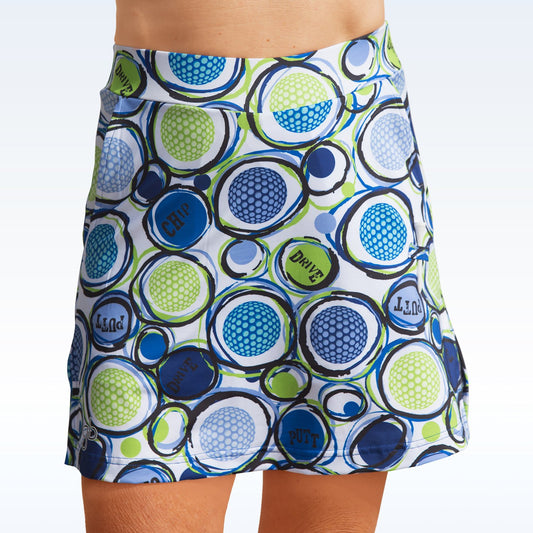 Woman models a white golf skort with a blue and green golf ball and golf term pattern. 
