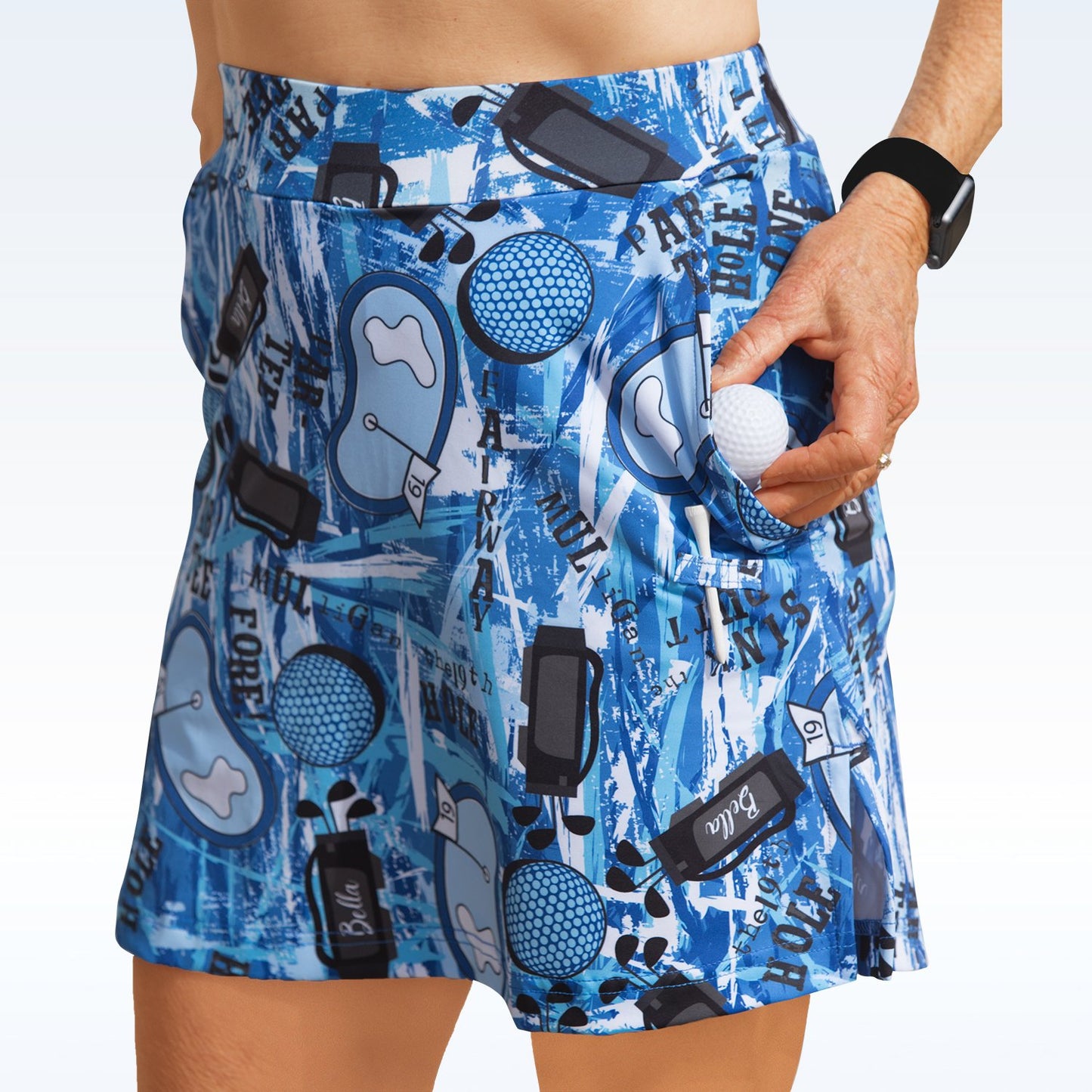 Woman models a blue golf skort with a fun, abstract golf course pattern. She stores a golf ball in the built-in pocket, ready for the next hole. 
