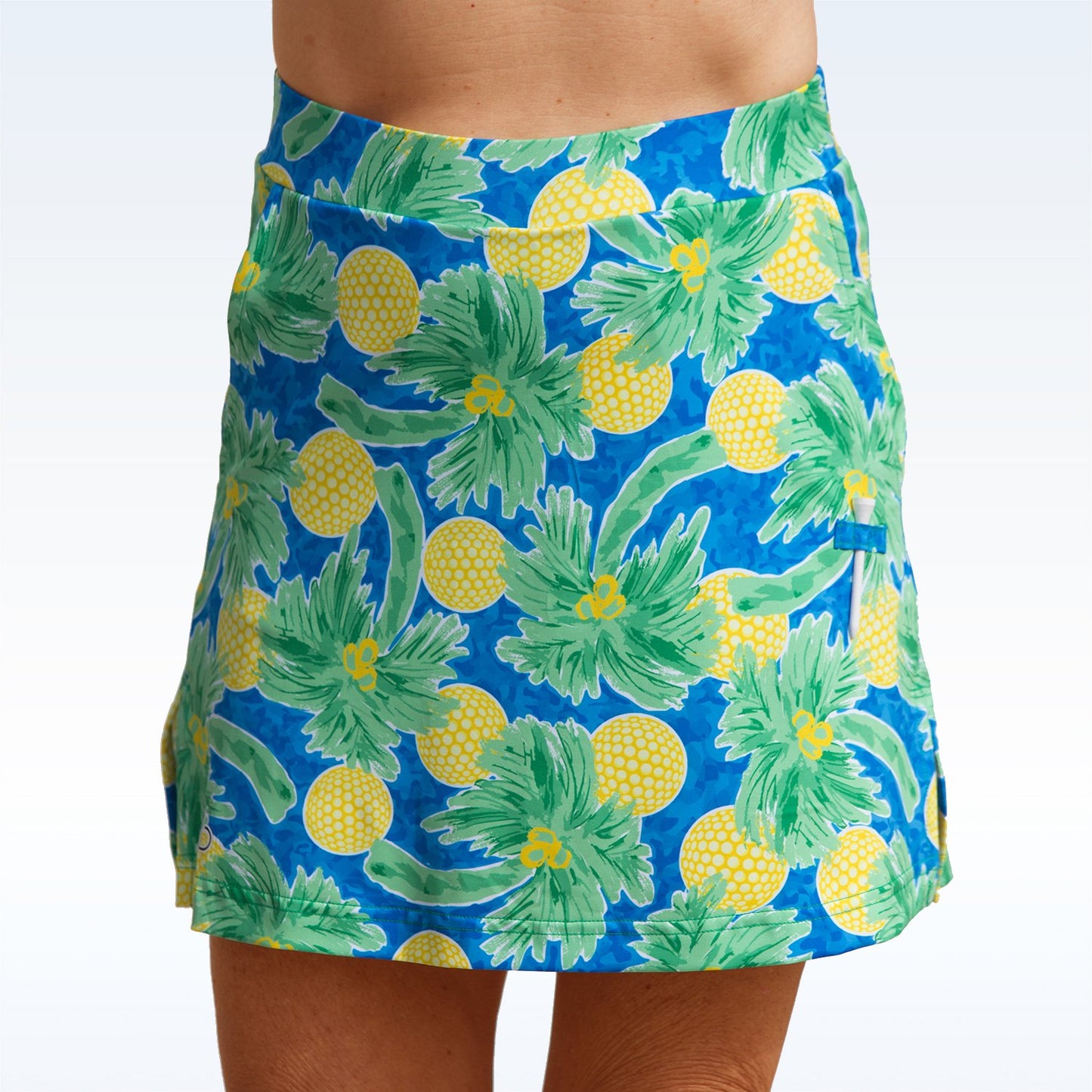Woman models a blue golf skort with a tropical print of palm trees and golf balls. 
