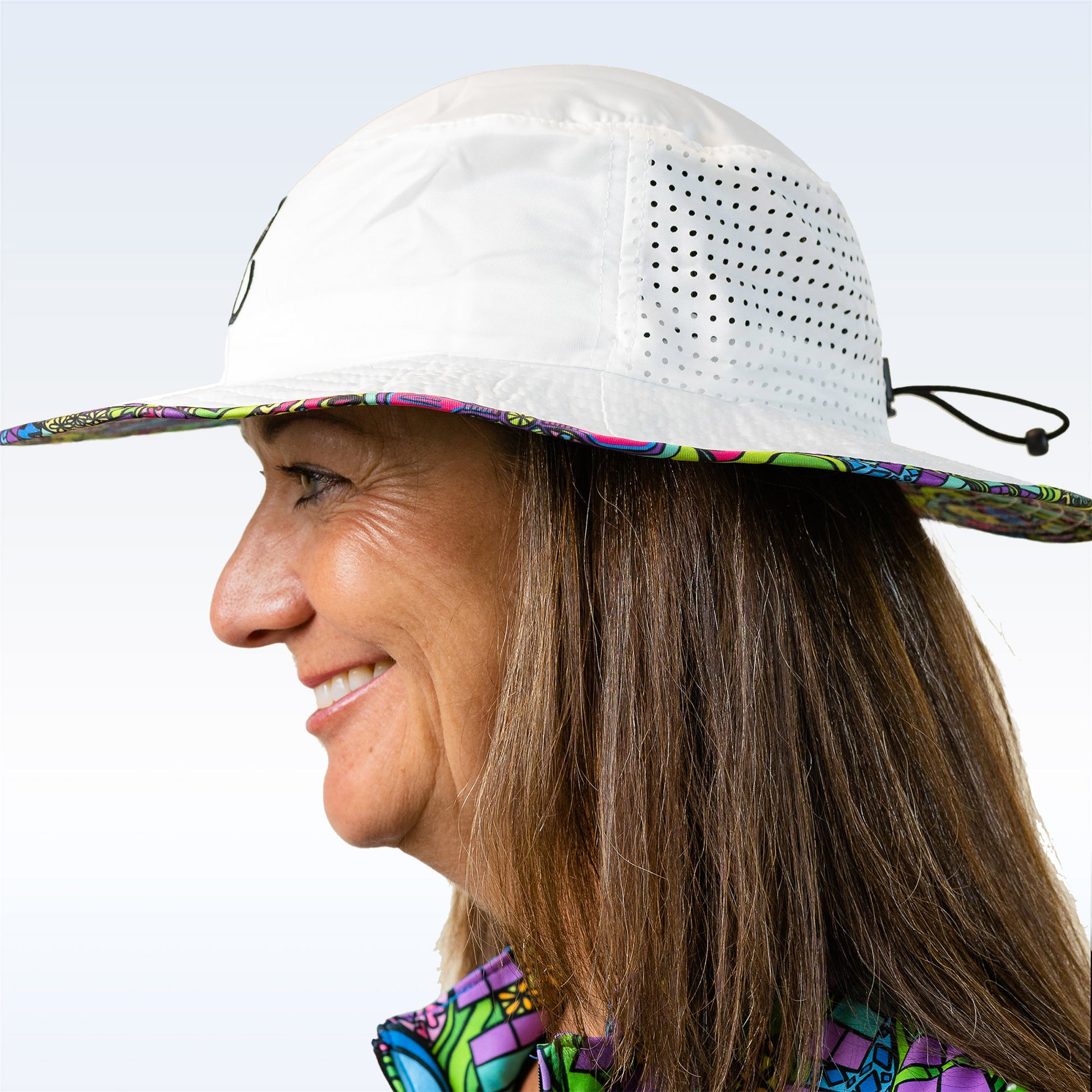 Woman smiles while wearing a white bucket hat with colorful floral trim and side ventilation. 
