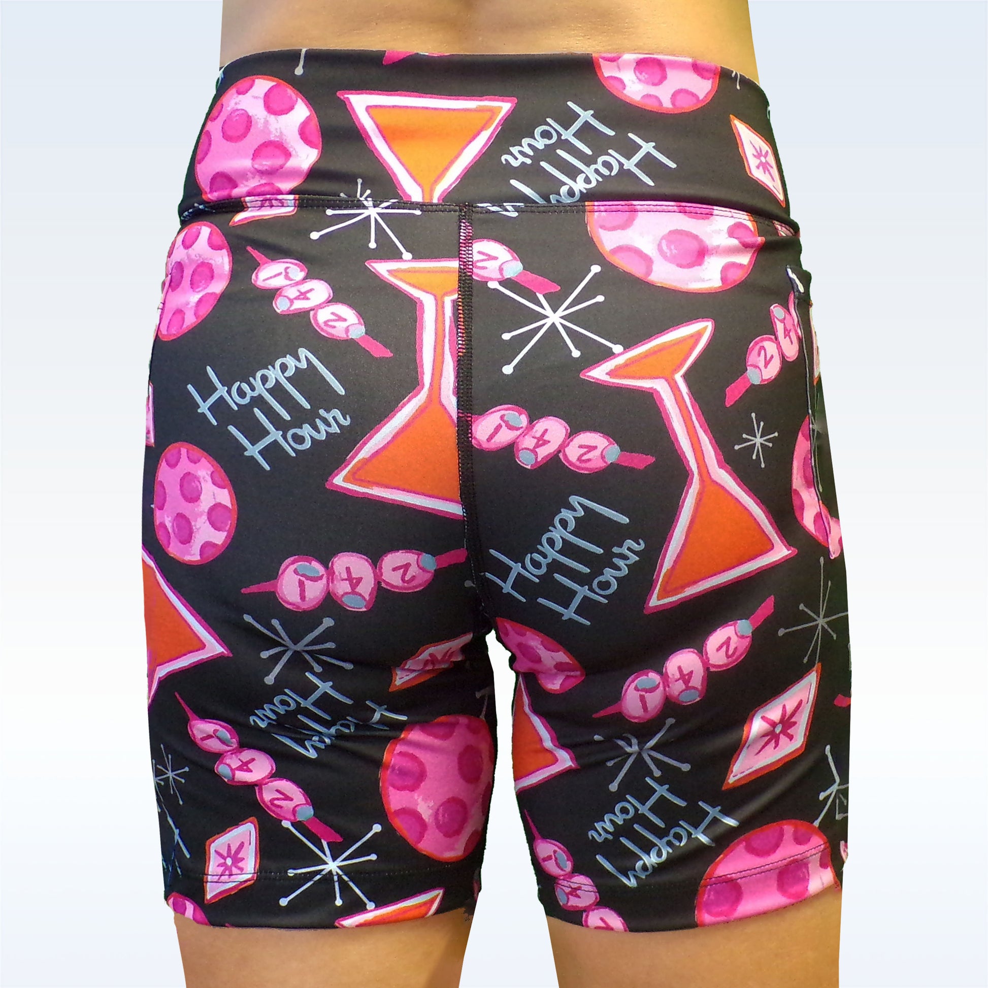 Woman models black athletic shorts with a pink and orange "Happy Hour" cocktail print. 
