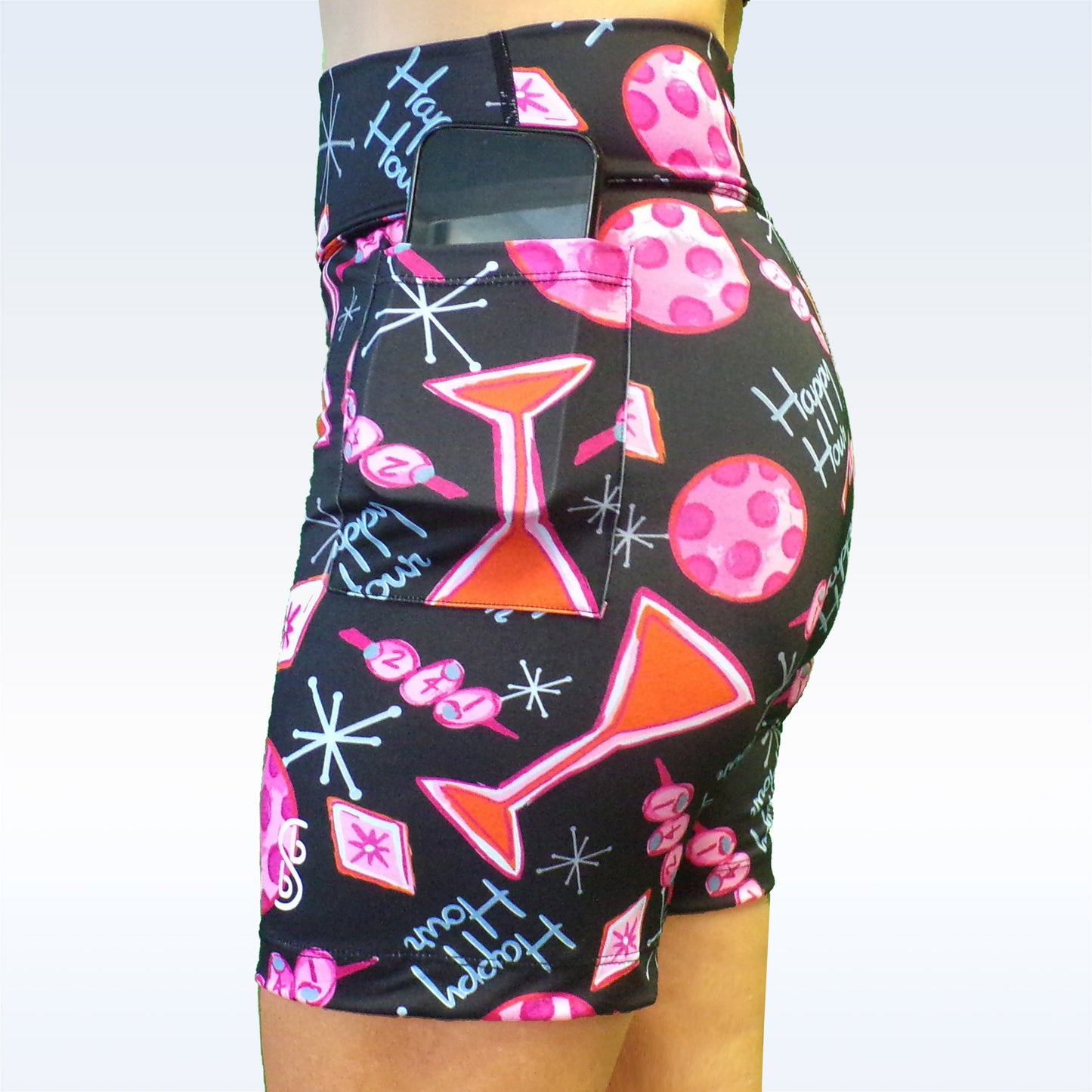 Woman models black athletic shorts with pink martini glass and "Happy Hour" print. Phone fits securely in back pocket. 
