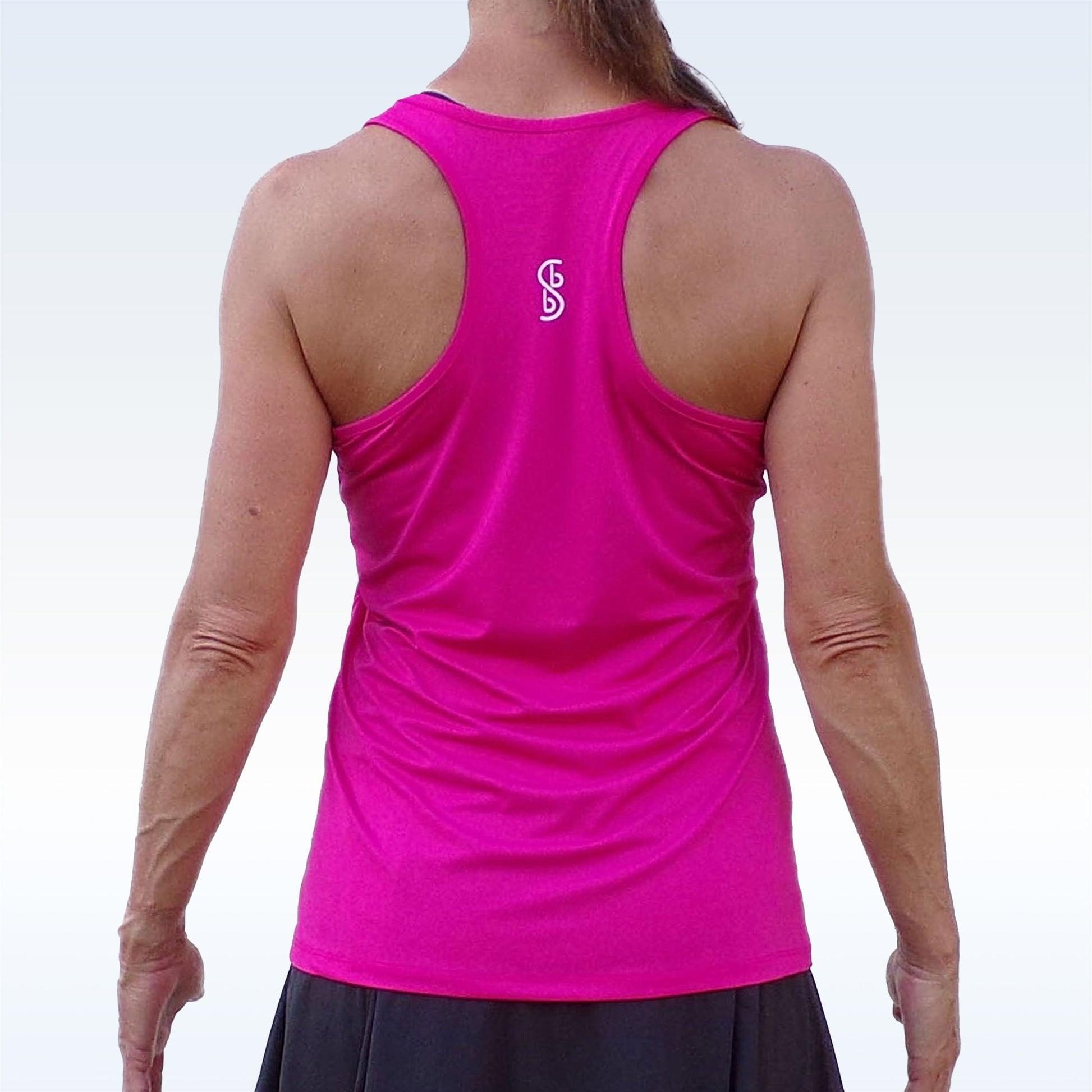 Woman models hot pink racerback tank top with white logo. 
